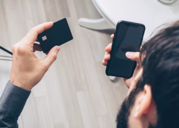 Close-up of man holding a smartphone and credit card, making an online payment indoors.