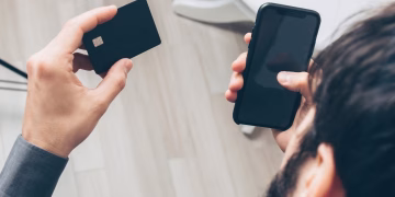 Close-up of man holding a smartphone and credit card, making an online payment indoors.