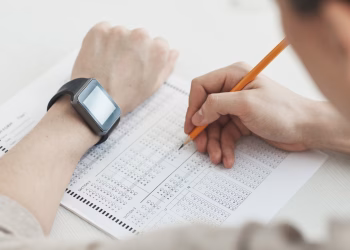 Close-up of a student writing answers on a test sheet with a pencil and smartwatch.