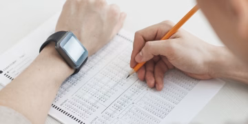 Close-up of a student writing answers on a test sheet with a pencil and smartwatch.