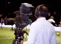 A cameraman filming a soccer match in a stadium, capturing the action on video.