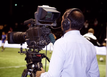A cameraman filming a soccer match in a stadium, capturing the action on video.
