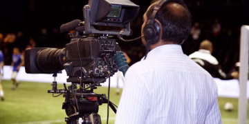 A cameraman filming a soccer match in a stadium, capturing the action on video.