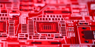 Contemporary red technical circuit board of modern electric machine with various numbers and symbols placed on blurred background in room