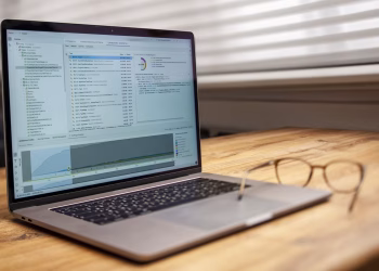 Modern laptop on a wooden desk displaying analytical software with eyeglasses nearby, indoor shot.