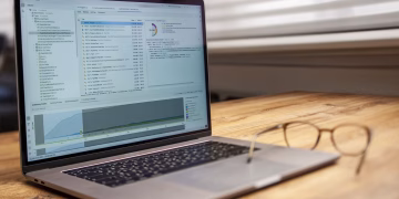 Modern laptop on a wooden desk displaying analytical software with eyeglasses nearby, indoor shot.