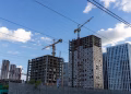 City skyline with modern buildings and construction cranes under a blue sky.