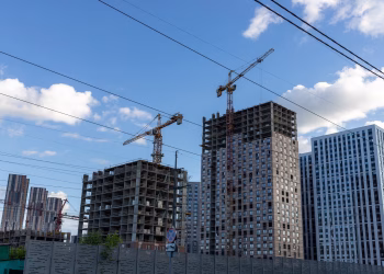 City skyline with modern buildings and construction cranes under a blue sky.