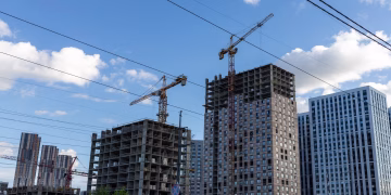 City skyline with modern buildings and construction cranes under a blue sky.