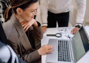 Businesswoman using laptop at office desk surrounded by colleagues, collaborating on project.
