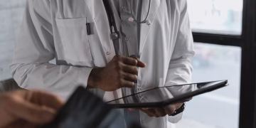 A professional medical practitioner holding a tablet, focused on work in a clinical setting.