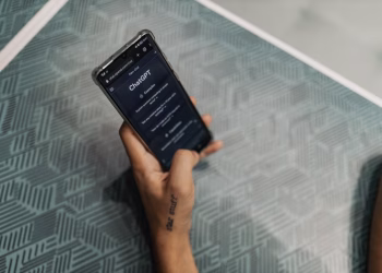 Close-up of a person holding a smartphone displaying the ChatGPT application interface on a patterned table.