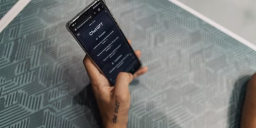 Close-up of a person holding a smartphone displaying the ChatGPT application interface on a patterned table.