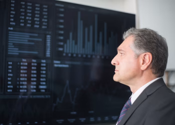 Mature businessman in corporate attire analyzing financial charts on a screen indoors.