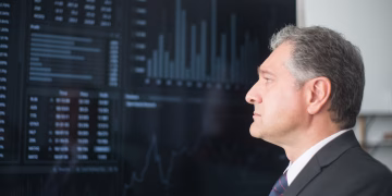 Mature businessman in corporate attire analyzing financial charts on a screen indoors.