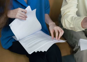People in professional attire reviewing important documents together on a sofa.