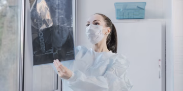 A medical professional examining an X-ray near a window in a clinical setting.