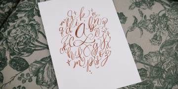 A beautiful handwritten alphabet on paper placed on a floral textile background, showcasing artistic calligraphy.
