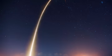 Spectacular long exposure of a rocket launch under a clear, starry night sky showcasing the trail.