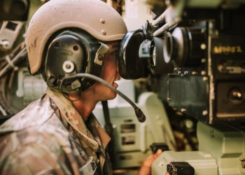 A soldier in uniform operates military equipment inside a vehicle, showcasing modern military technology.