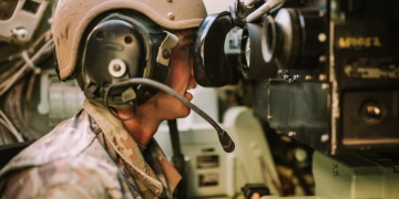 A soldier in uniform operates military equipment inside a vehicle, showcasing modern military technology.