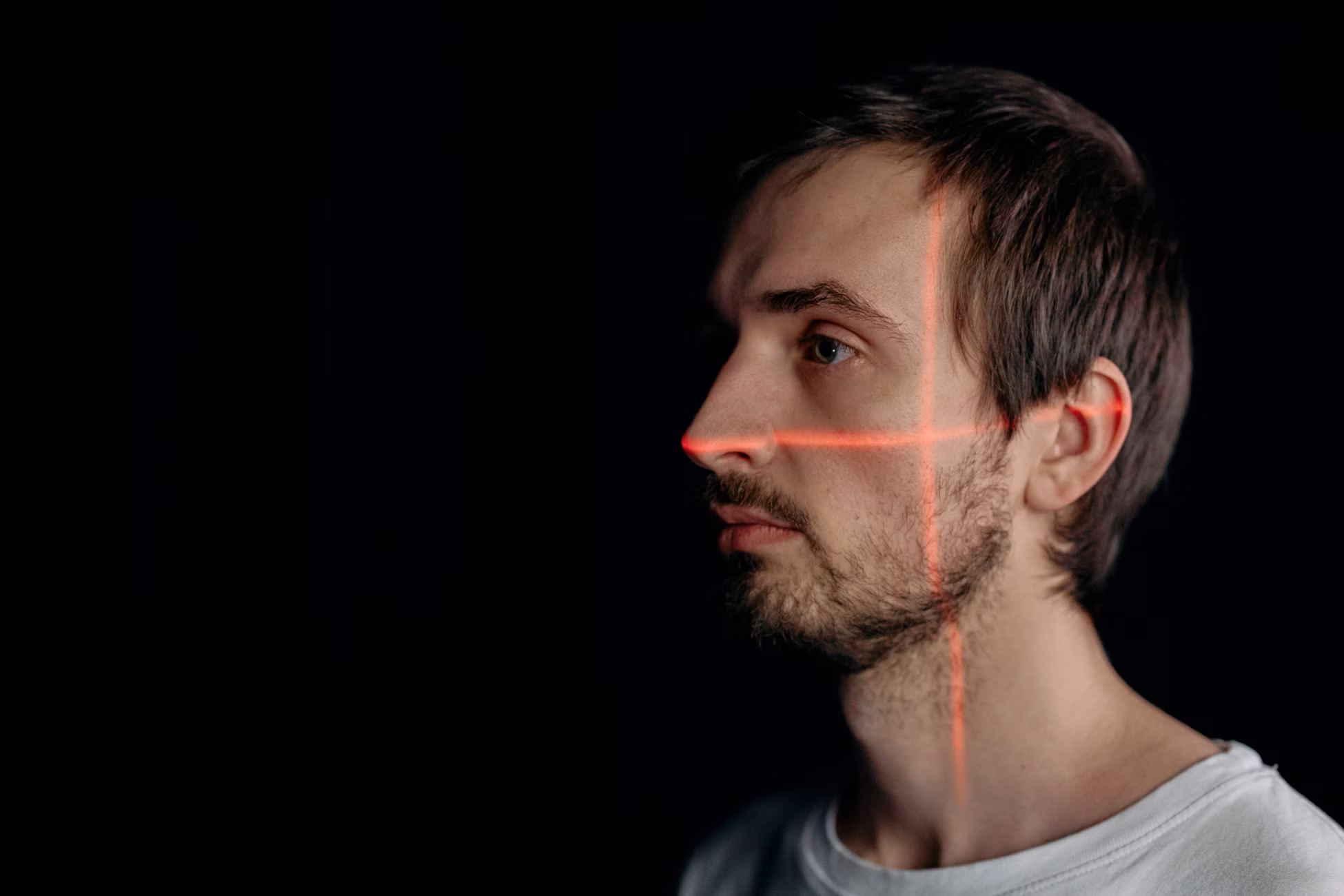 A side profile of a man with facial recognition laser scan on his face against a black background.