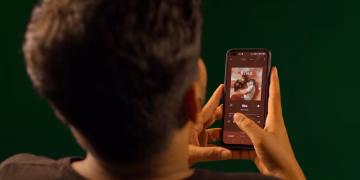 A person using a smartphone to stream music from a streaming service app indoors.