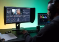 Man editing footage on dual monitors in a modern studio setting.