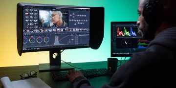 Man editing footage on dual monitors in a modern studio setting.