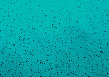 Close-up of water droplets on a teal glass window, capturing the beauty of rain.