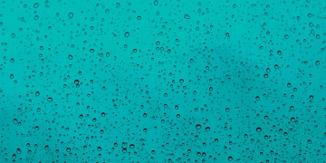 Close-up of water droplets on a teal glass window, capturing the beauty of rain.