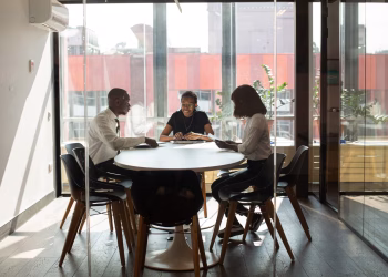 Three professionals collaborating in a modern office boardroom setting during daylight.