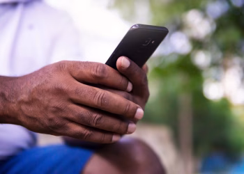 A close-up of a man's hands holding a smartphone in a park setting, showcasing technology use.