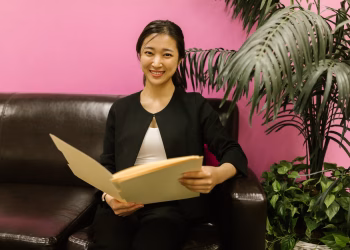Young woman in business attire holding a folder on a couch with vibrant background.