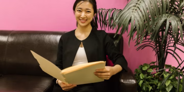 Young woman in business attire holding a folder on a couch with vibrant background.