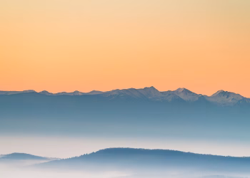 A peaceful view of misty mountains during sunrise with soft pastel colors.