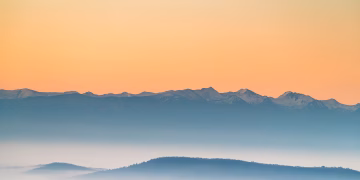 A peaceful view of misty mountains during sunrise with soft pastel colors.