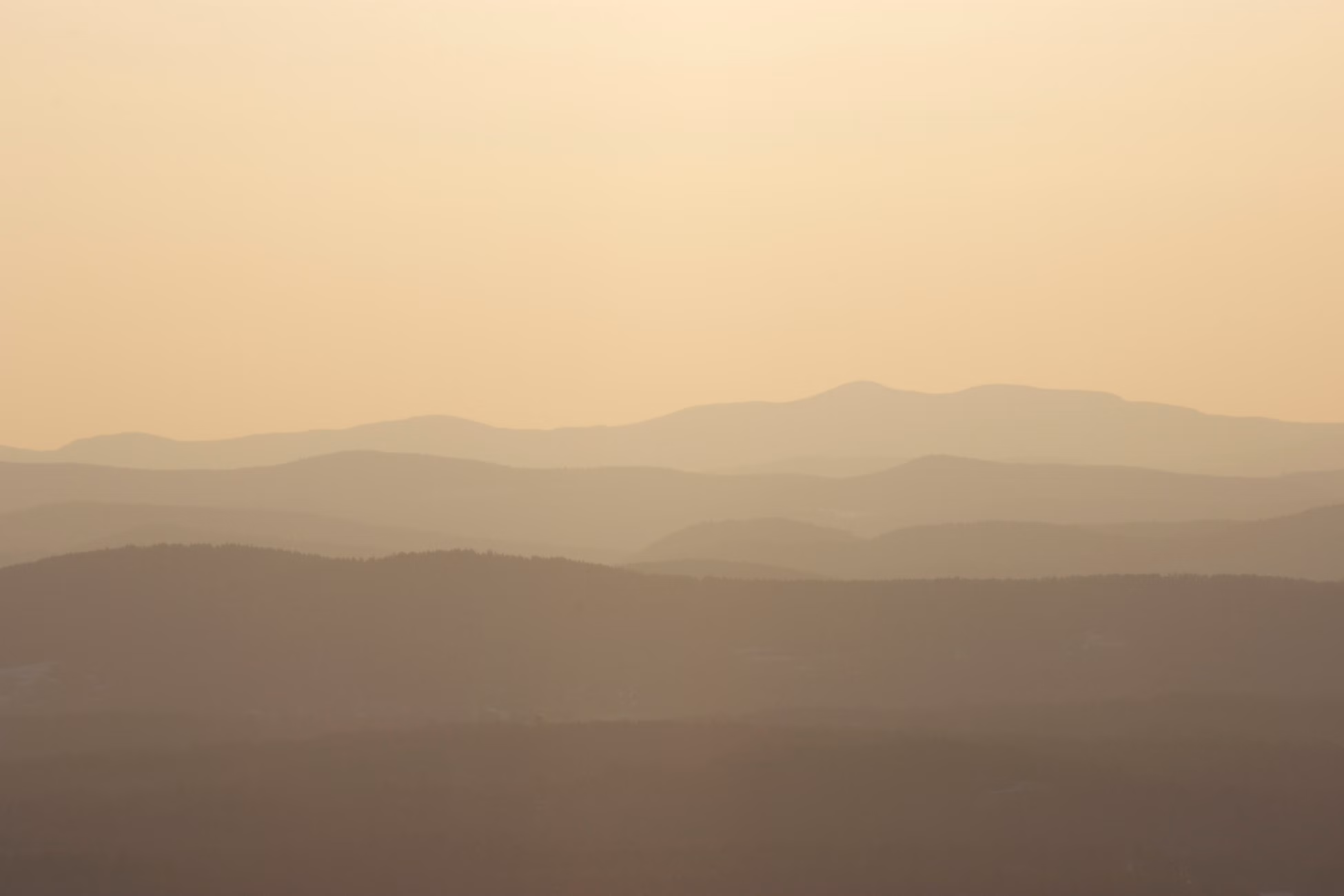 Peaceful dawn landscape with layers of misty mountain ranges under a warm glow.