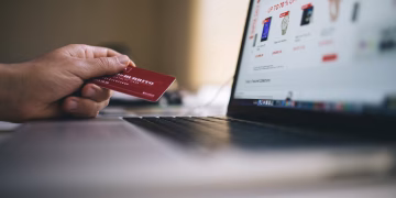 Person holding a credit card while shopping online on a laptop, indicating ecommerce transactions.