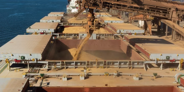 Aerial view of a cargo ship loading grain at a bustling industrial port by the sea.