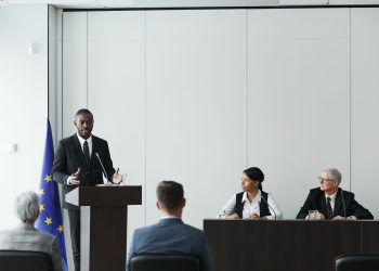 Business meeting featuring diverse professionals discussing important topics with a speaker at the podium indoors.