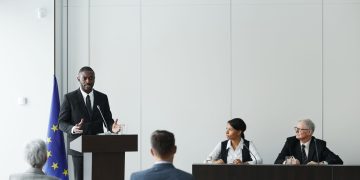 Business meeting featuring diverse professionals discussing important topics with a speaker at the podium indoors.