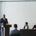 Business meeting featuring diverse professionals discussing important topics with a speaker at the podium indoors.
