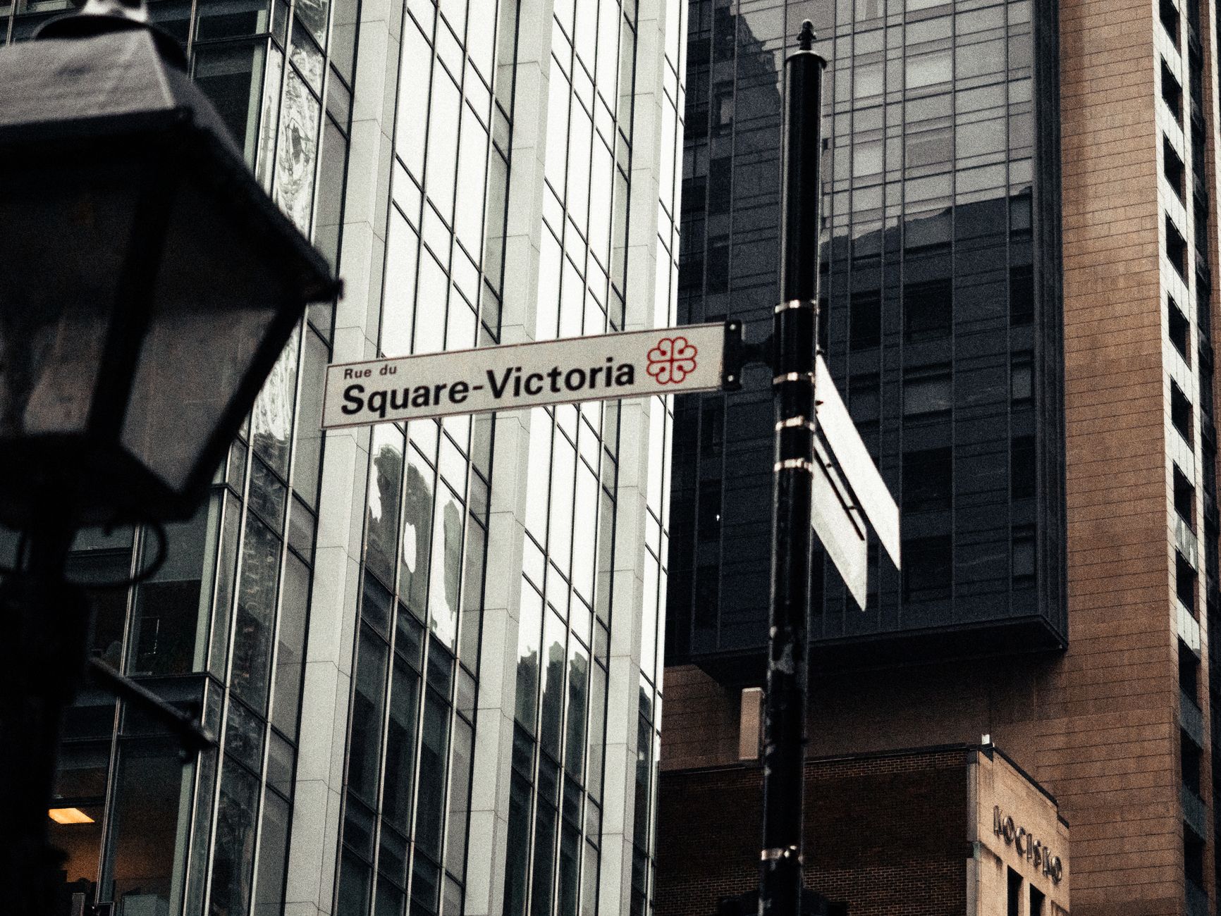 Street sign for Rue du Square-Victoria in Montreal, set against a backdrop of modern architecture.