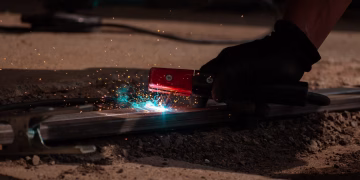 Detailed close-up of welding process with tool, sparks, and glowing metal.