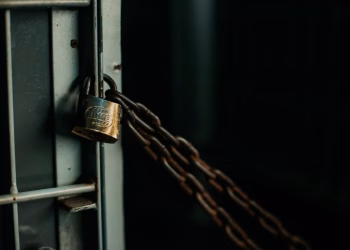 An artistic close-up photo of a faded padlock securing a chain on a metal door, symbolizing security.