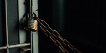 An artistic close-up photo of a faded padlock securing a chain on a metal door, symbolizing security.