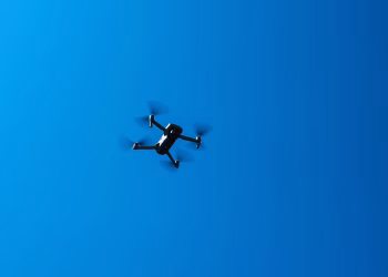 A black drone flying high in a clear blue sky, showcasing modern technology and flight capabilities.