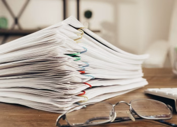 Close-up of a stack of office papers on a desk with glasses, emphasizing organization.