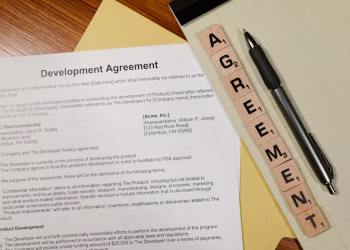 Close-up of a development agreement document with pen and Scrabble tiles spelling 'AGREEMENT.'